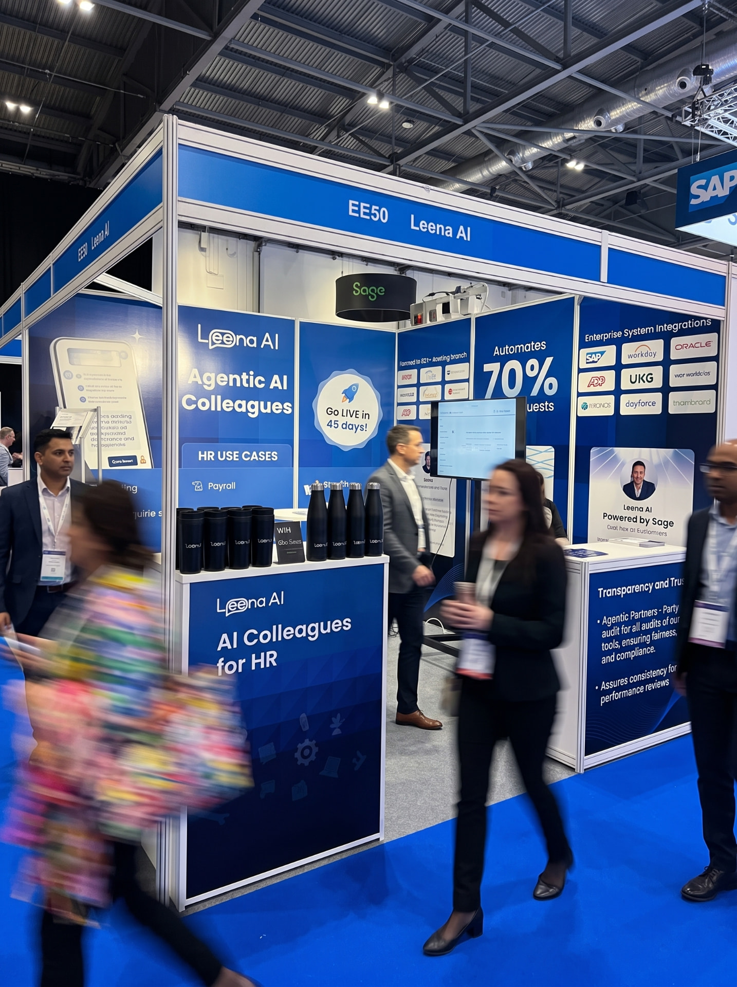 The Leena AI stand — blue panels with Agentic AI Colleagues branding, a merch counter and visitors in the aisle