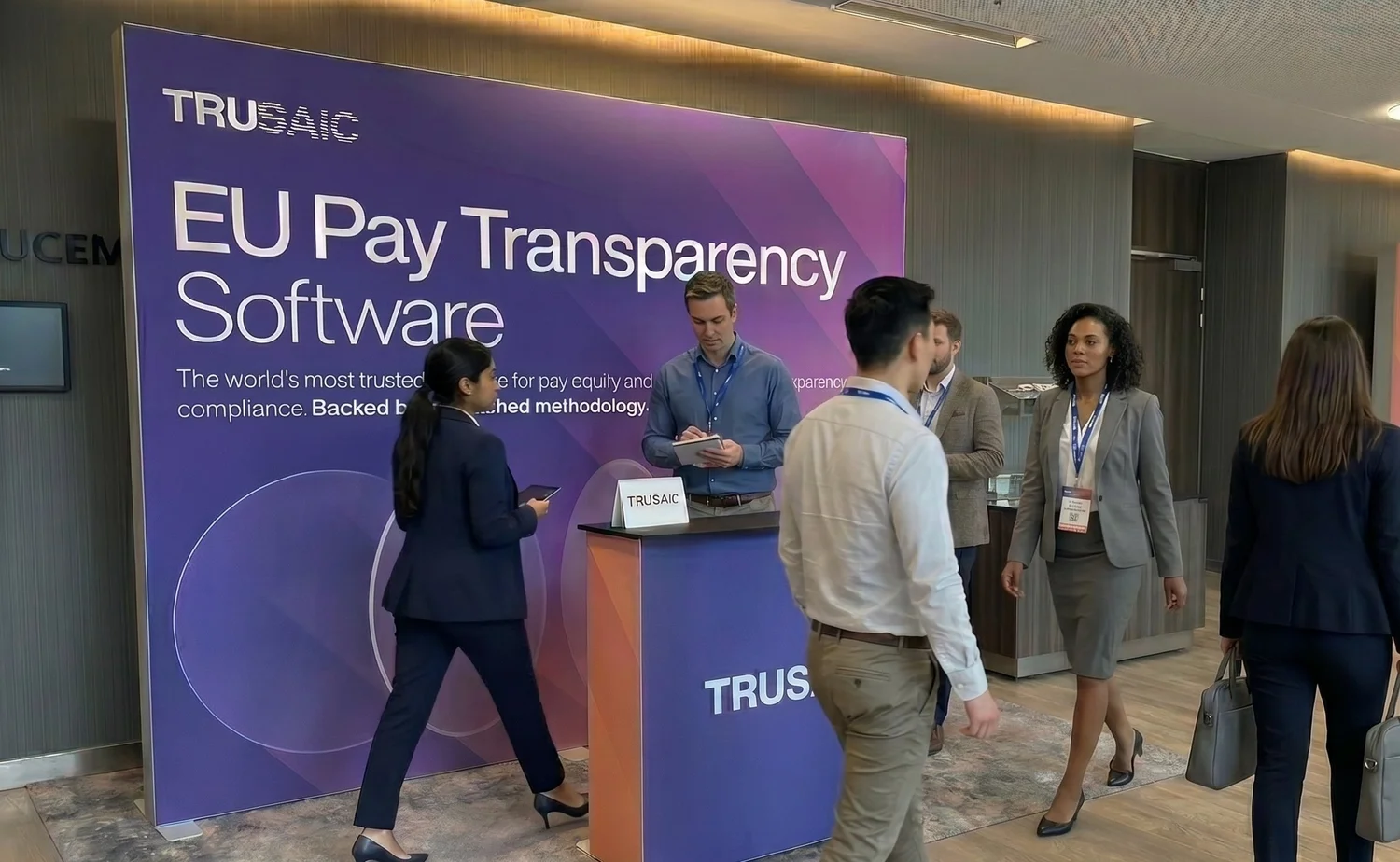 The Trusaic stand — a purple EU Pay Transparency Software backdrop with a branded counter, staff and visitors